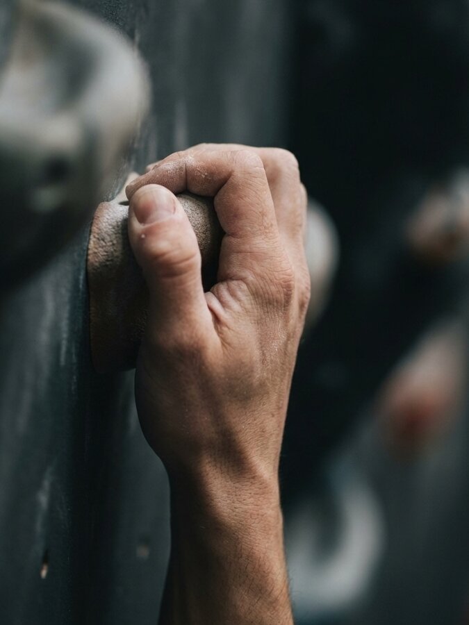 Primer plano de una mano agarrando una regleta, con las venas del antebrazo marcadas por la tensión